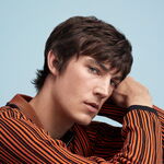 Mann mit locker texturiertem braunem Haar und beweglichem Styling vor hellblauem Hintergrund